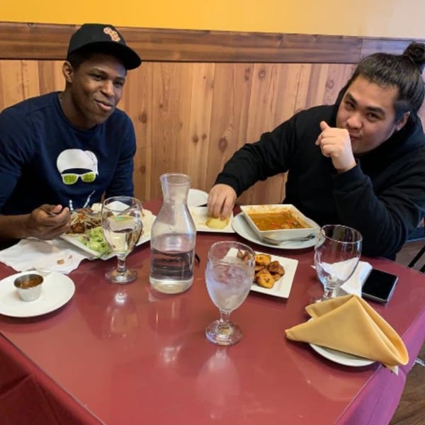Two men enjoying African cuisine at Drelyse African Restaurant, with dishes like stew and plantains.