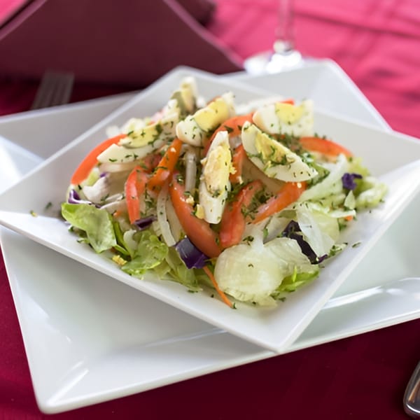 A fresh garden salad with lettuce, tomatoes, onions, and hard-boiled egg slices on a white plate.