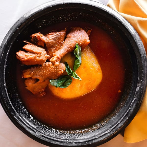 Drelyse African Restaurant's chicken and fufu in a rich red stew, garnished with green leaves.