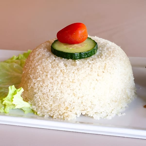 Molded white rice or couscous, garnished with a cucumber slice and a cherry tomato, on a white plate.