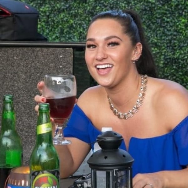 A smiling woman in a blue dress holds a glass of red wine at Drelyse African Restaurant.