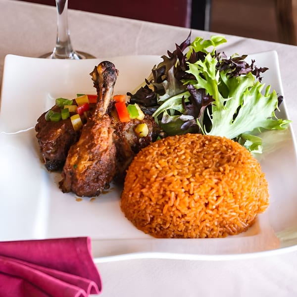 African jollof rice with chicken drumsticks topped with diced peppers and a side salad.