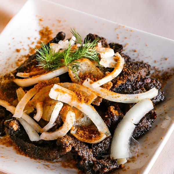 African dish with dark meat, sliced white onions, and orange seasoning, garnished with dill.