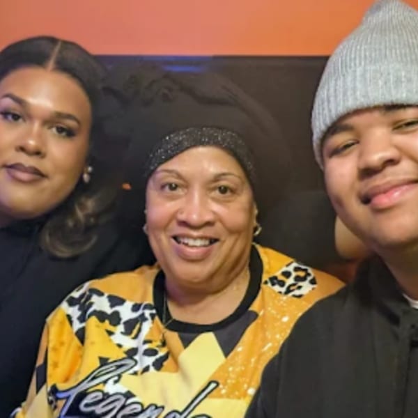 Three people, two smiling, one wearing a gray beanie, posing for a close-up photo.