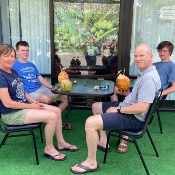 Four people sit at an outdoor table with coconut drinks, in front of Drelyse African Restaurant.